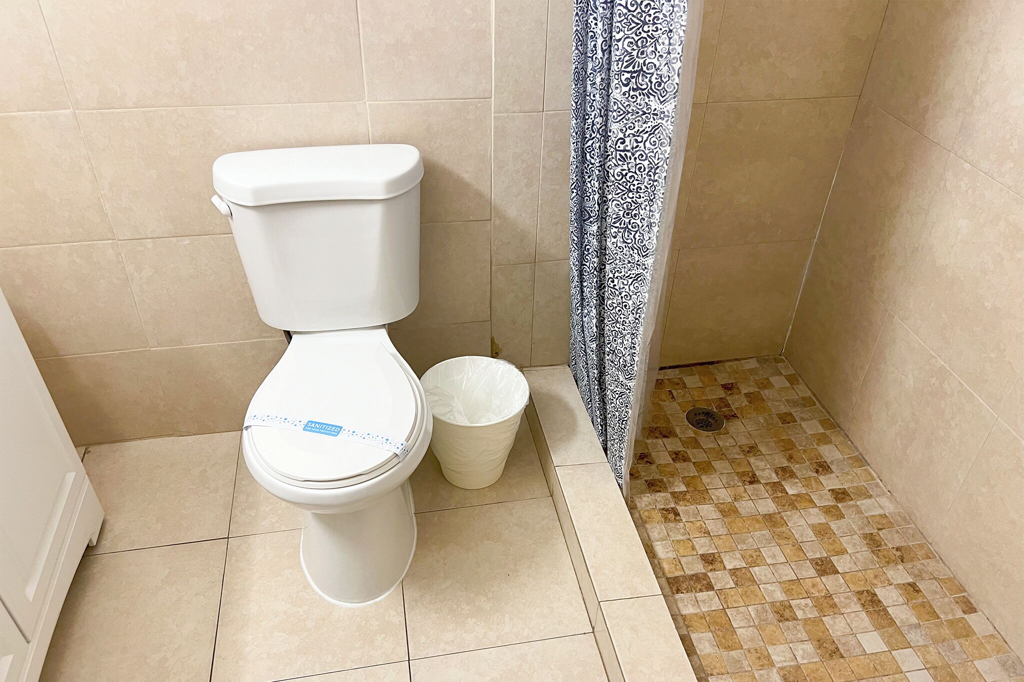 Des toilettes avec un abattant blanc et une poubelle blanche à côté.