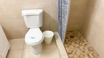 A toilet with a white lid and a white trash bin next to it.