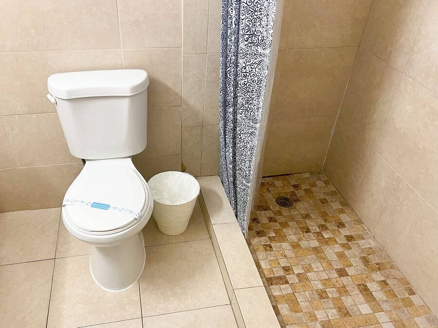A toilet with a white lid and a white trash bin next to it.