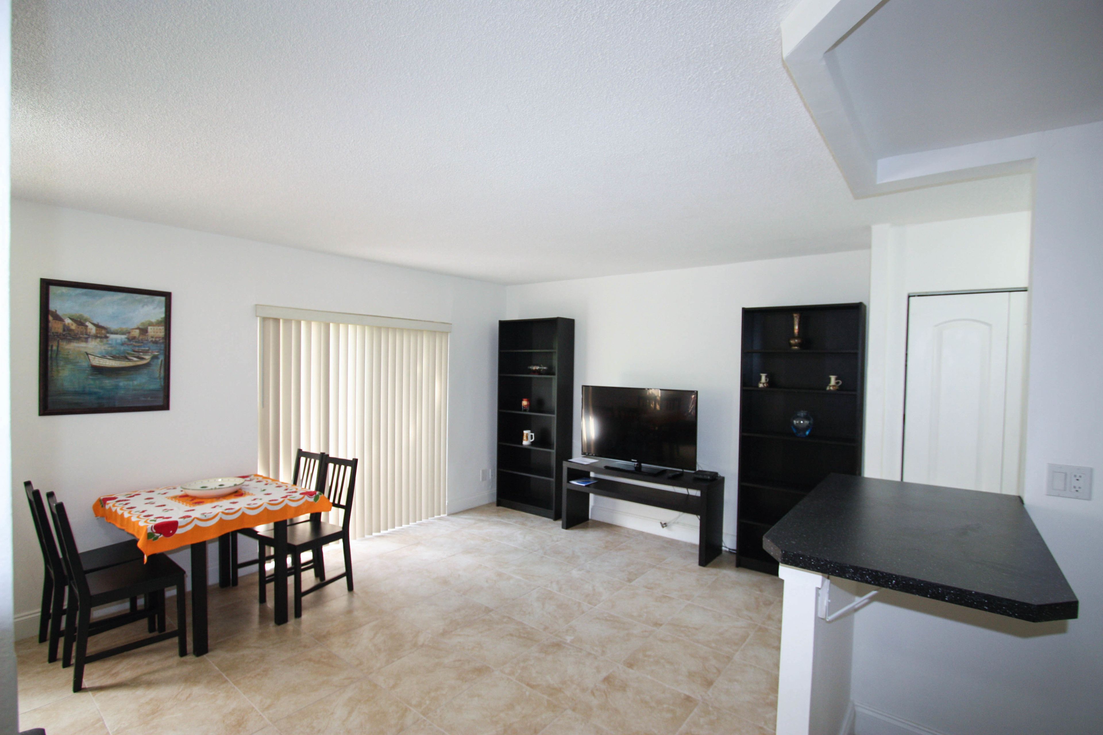A living room with a dining table, chairs, a TV, and a kitchen counter.