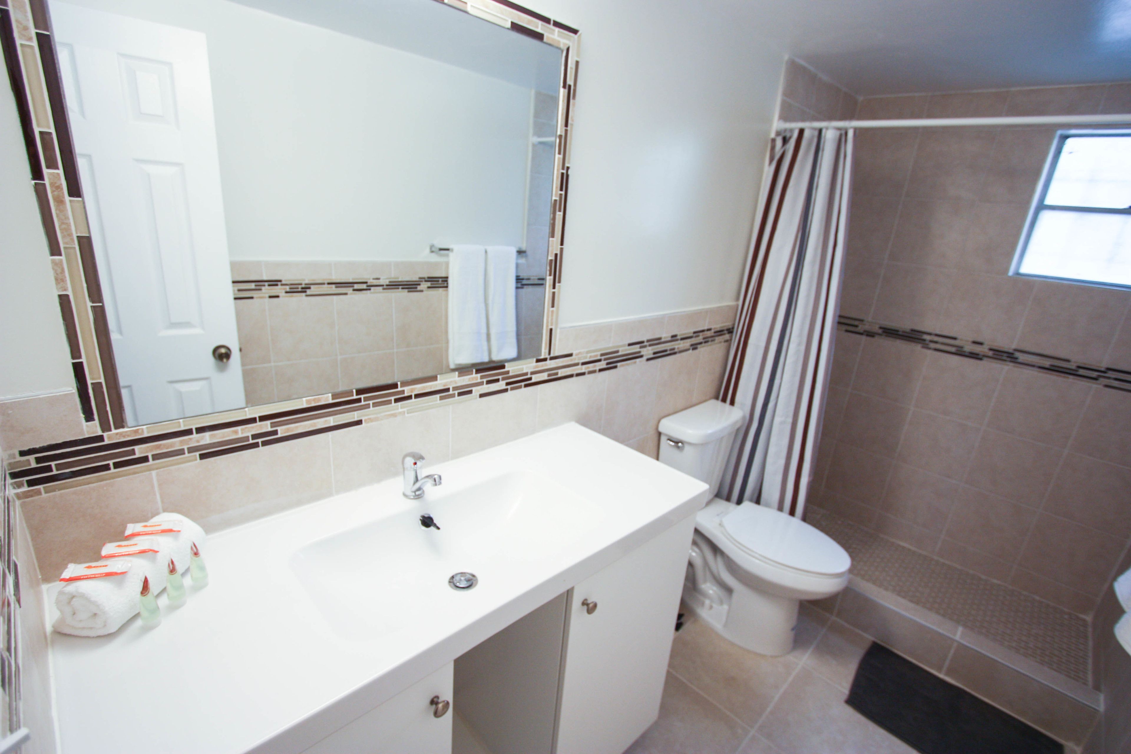 Une salle de bain avec un lavabo blanc, des toilettes, un espace douche et un miroir orné d’un cadre décoratif.