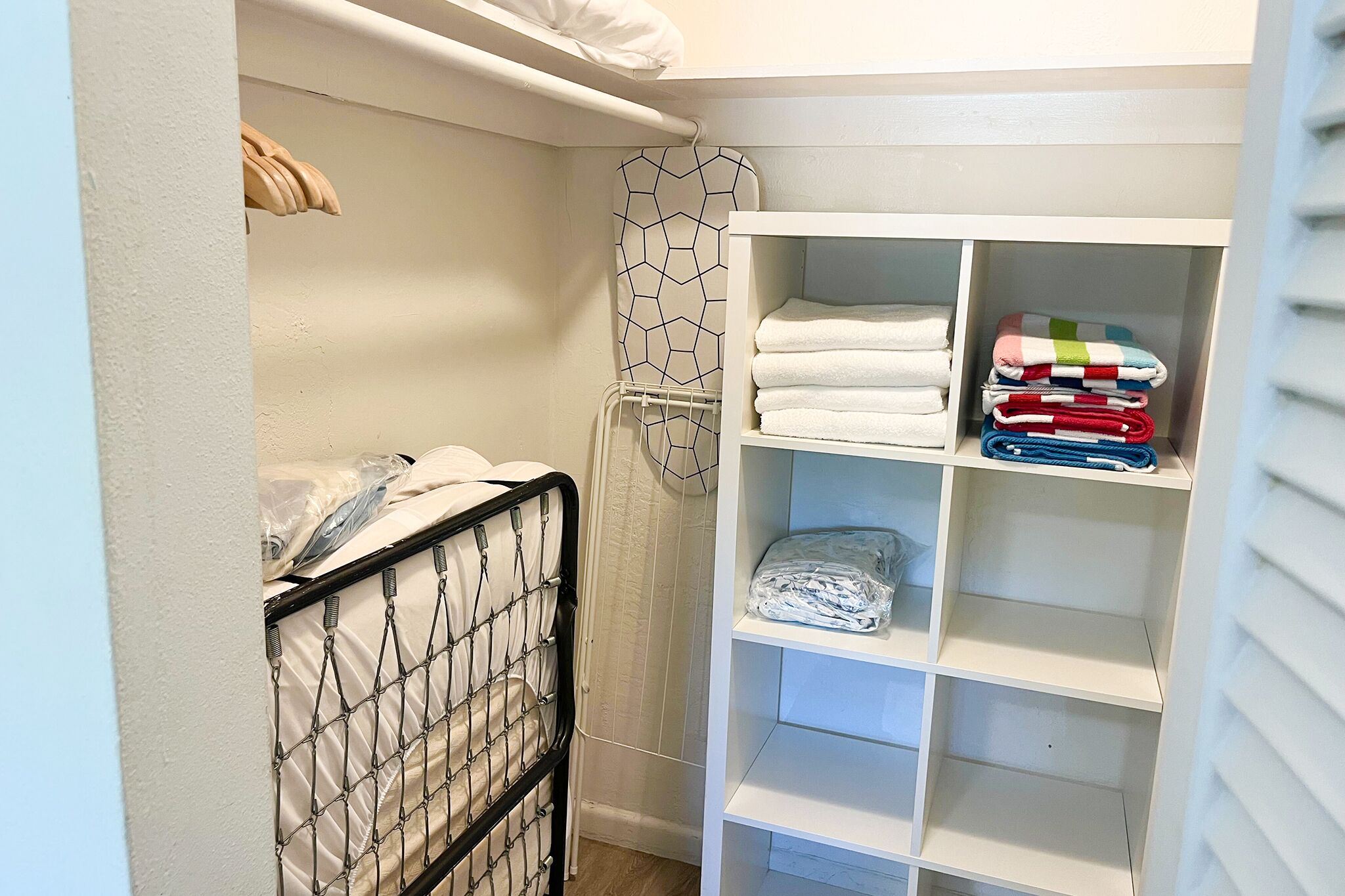 A bedroom with a bed, a closet with shelves, and a hanging rack.