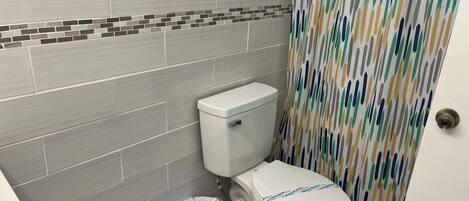 A bathroom with a toilet, a trash bin, and a shower curtain.