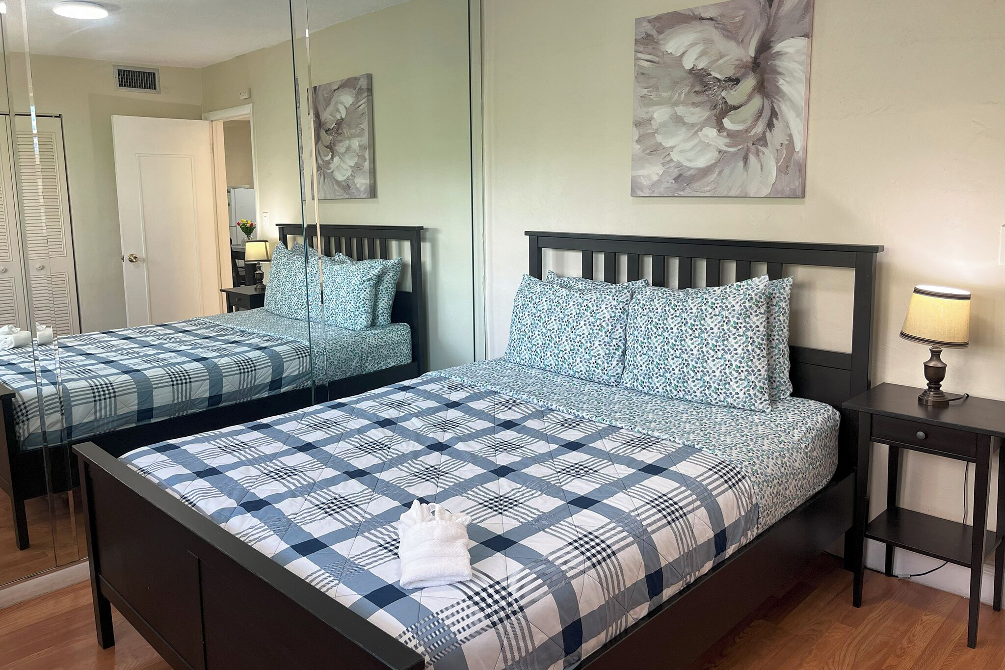 Een hotelkamer met twee bedden, elk met een beddekleed met dessin en passende kussens. Er is een nachtkastje met een lamp en een spiegel aan de muur.