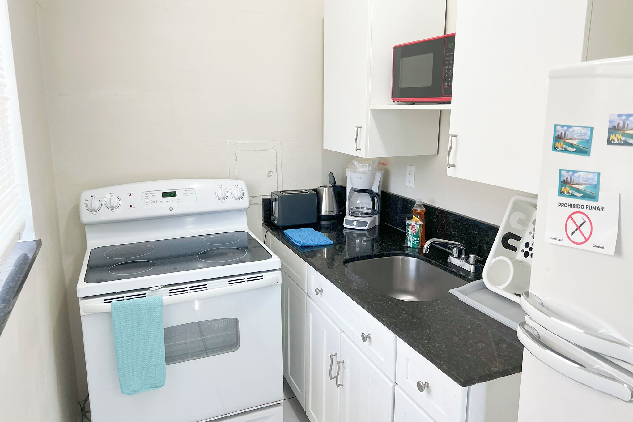Una cocina compacta con estufa blanca, microondas, cafetera y lavaplatos.