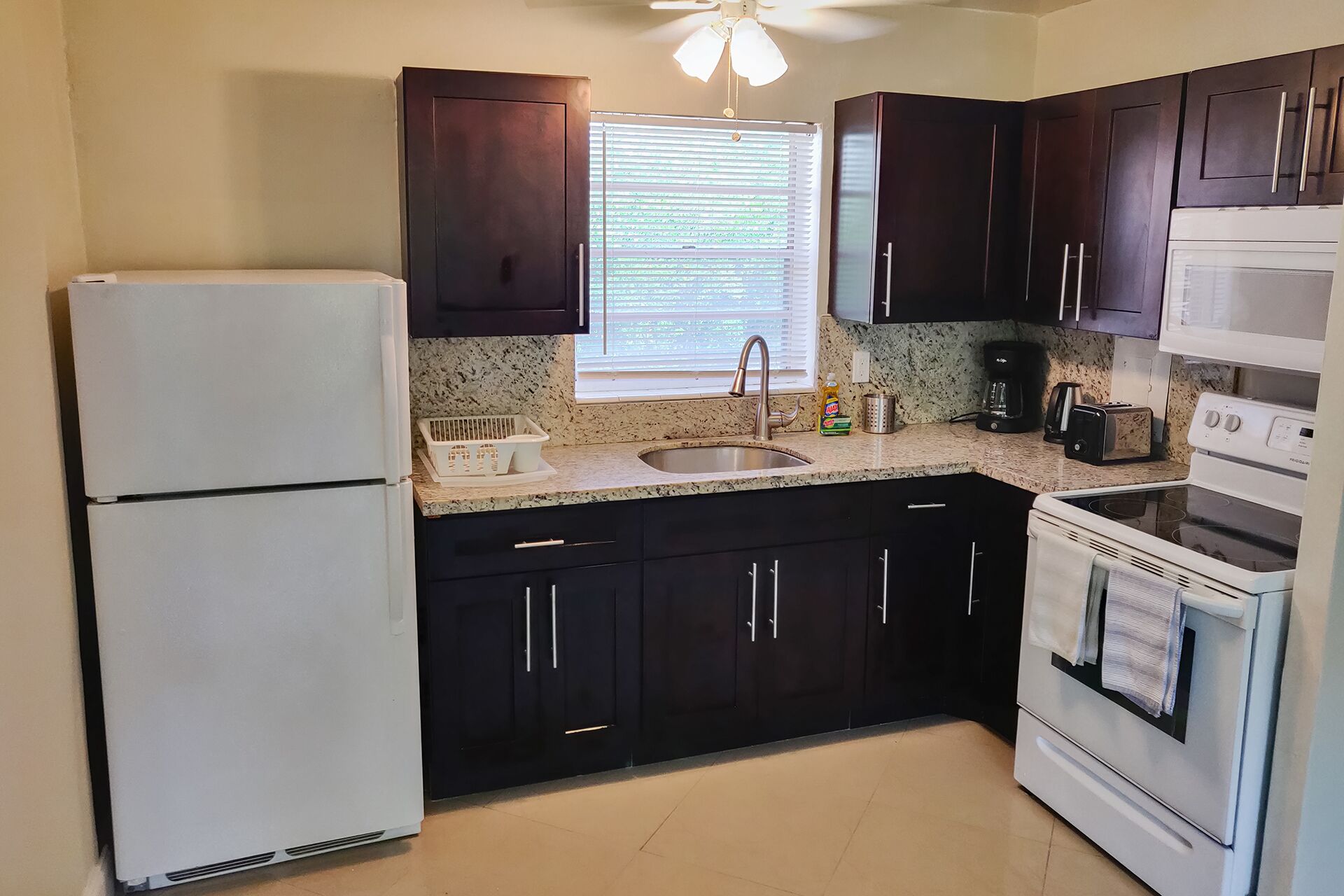 A kitchen with dark cabinets, a white refrigerator, a sink, a stove, and a ceiling fan.