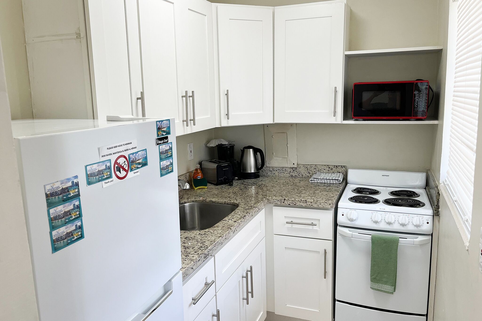 A compact kitchen with white cabinets, a white refrigerator, a microwave, a stove, and a sink.