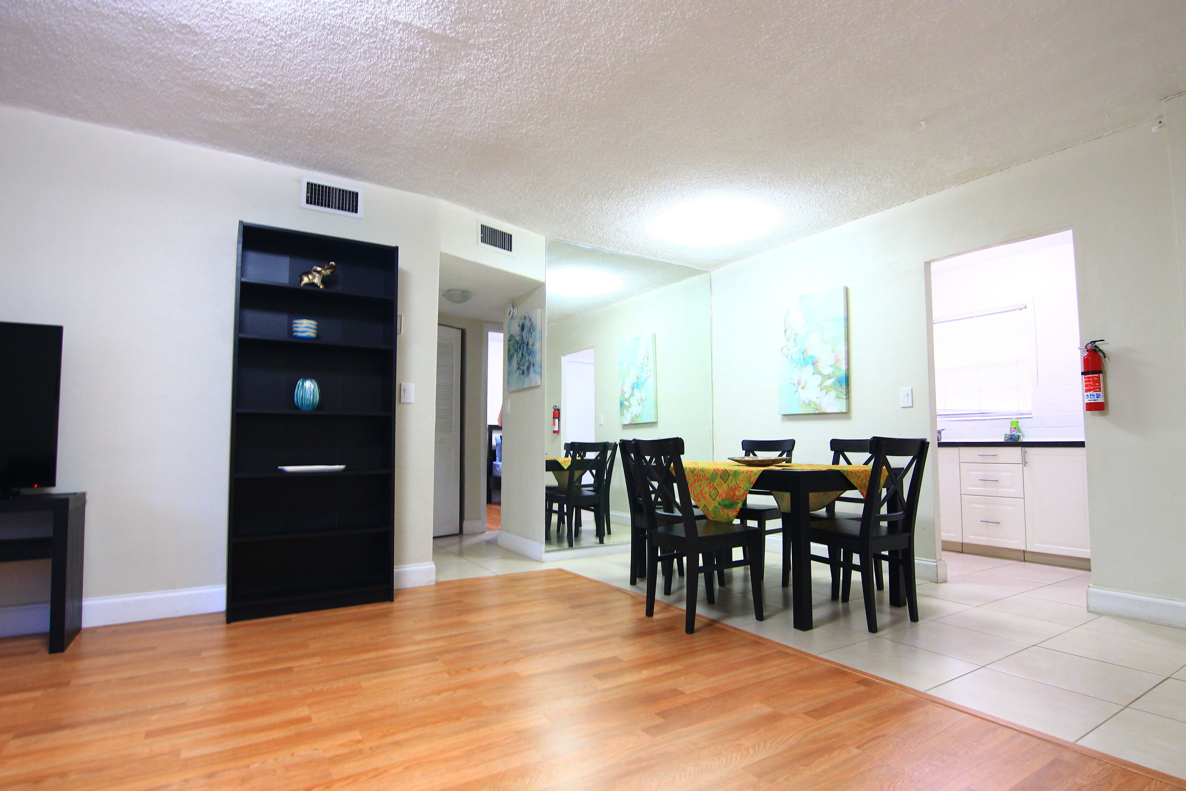 A dining area with a table and chairs, a black entertainment unit, and a kitchen area with cabinets and a window.