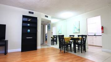 Un comedor con mesa y sillas, un mueble de entretenimiento negro y una zona de cocina con armarios y una ventana.