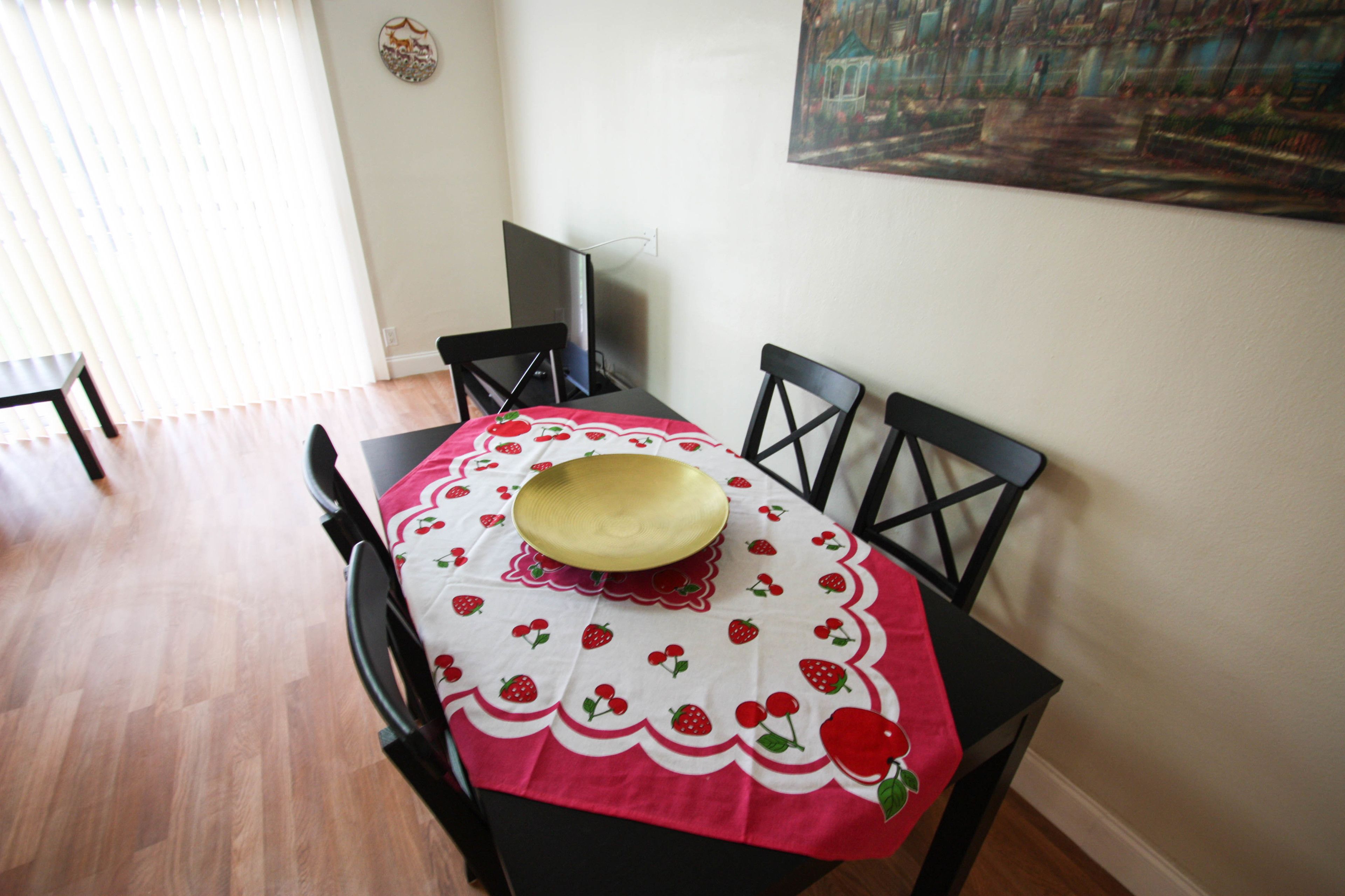 Una mesa de comedor con mantel rojo y blanco, un cuenco dorado y sillas negras.