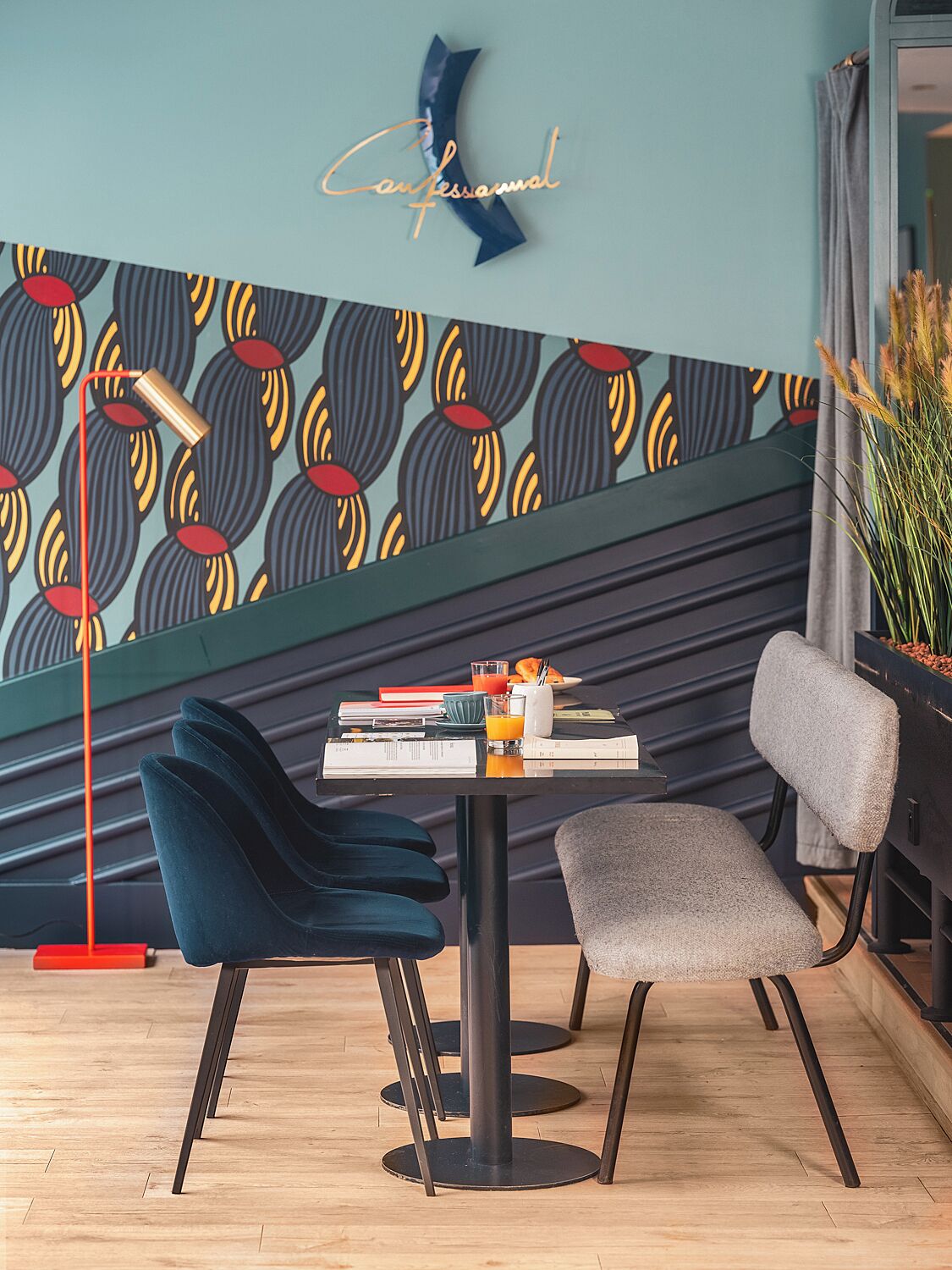 A modern dining area with a patterned wall, a table with books and a glass of orange juice, and two chairs.