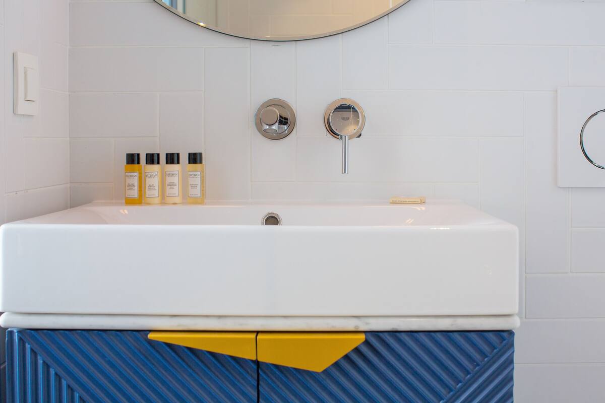 A bathroom with a white sink, two round mirrors, and three bottles of lotion on the counter.