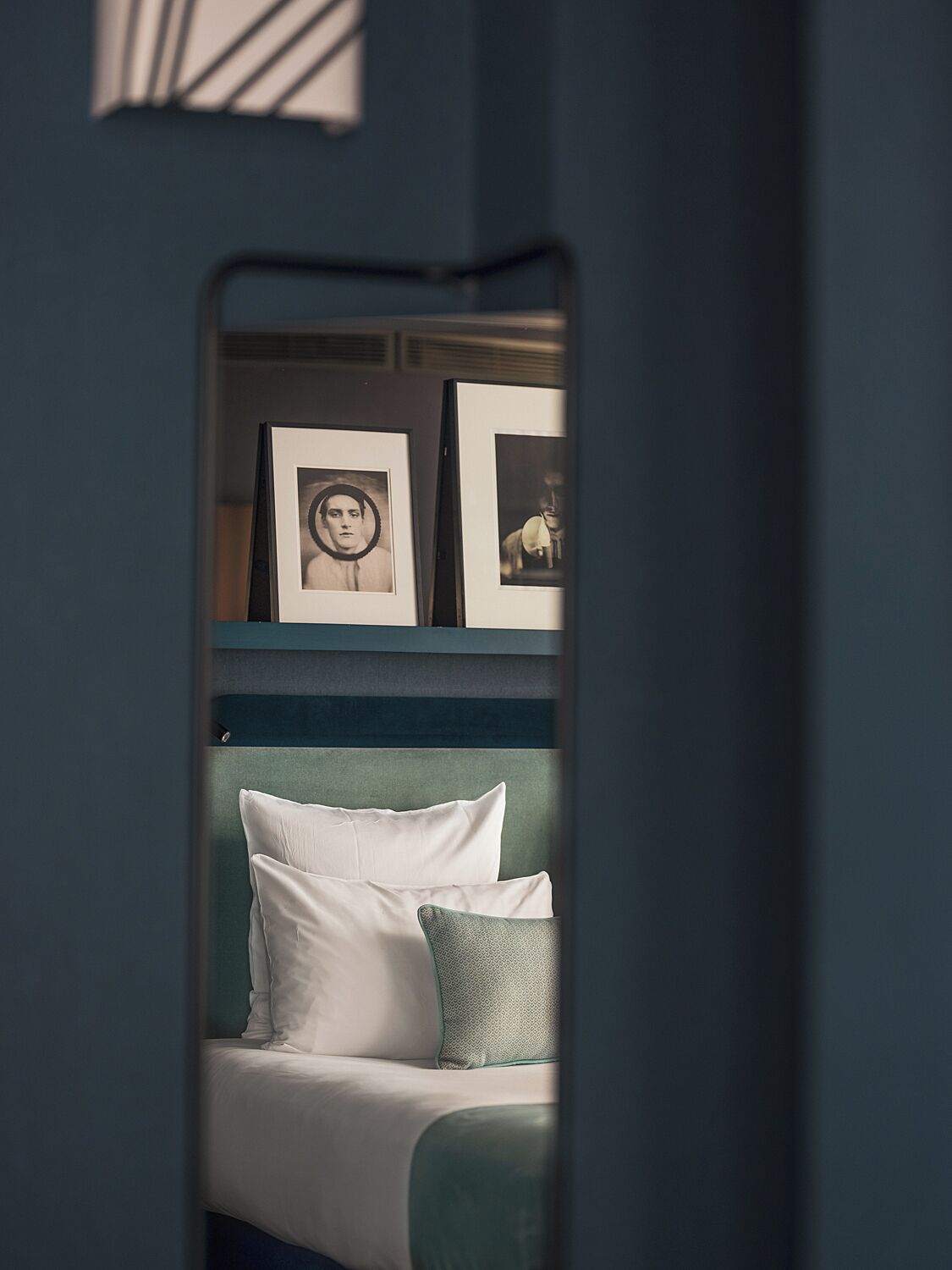 A room with a bed, pillows, and framed pictures on a shelf.