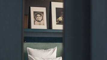 A room with a bed, pillows, and framed pictures on a shelf.