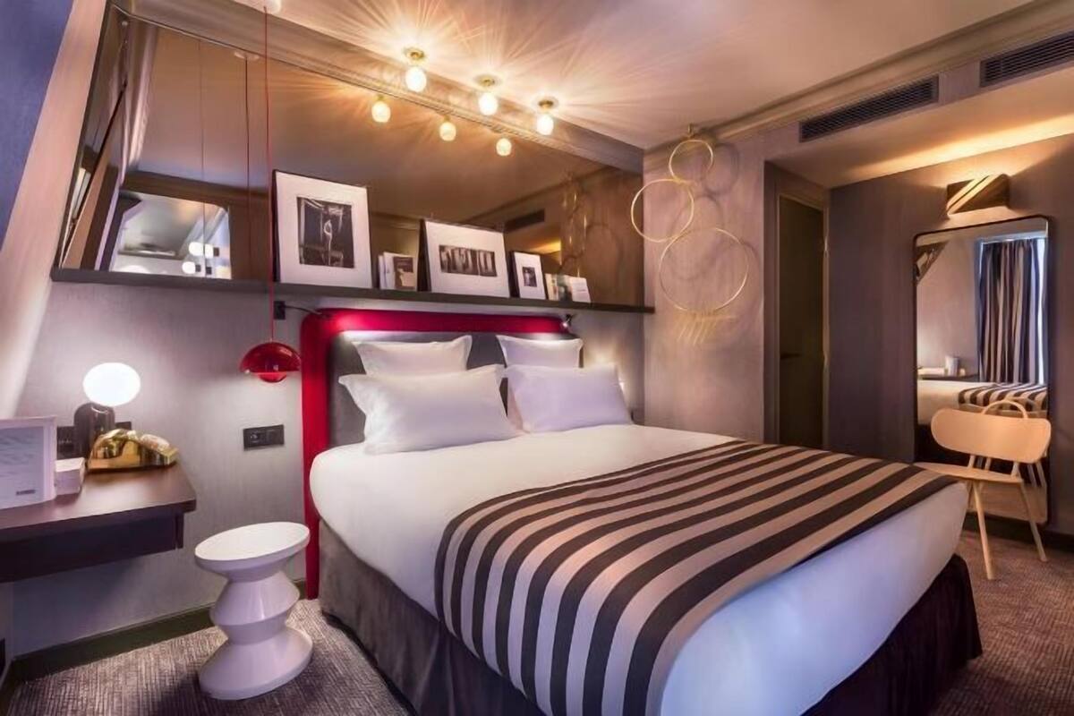 A hotel room with a bed, bedside table, lamp, and a mirror.