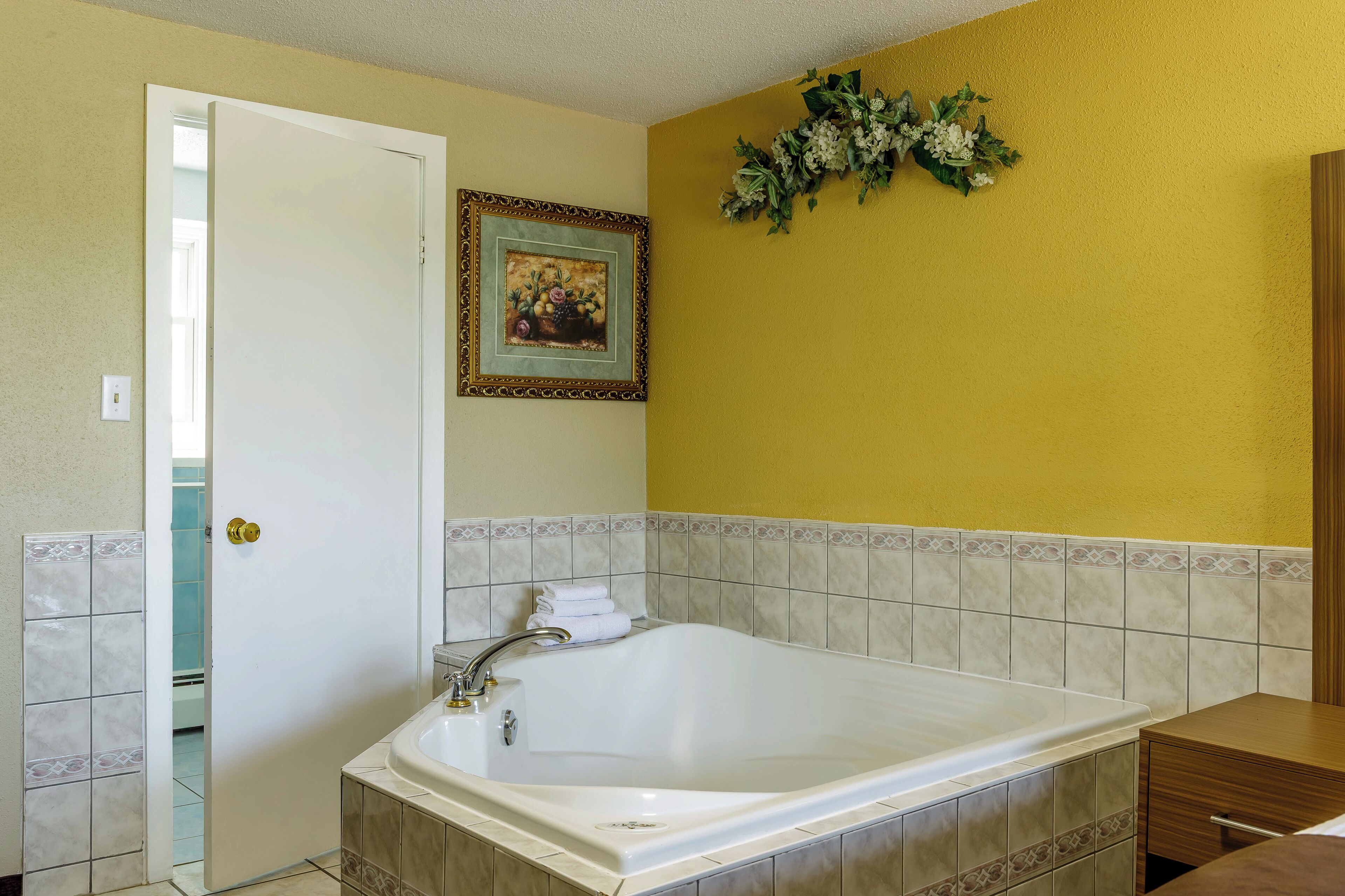 A bathroom with a large bathtub, a door, a framed picture on the wall, and a decorative plant.