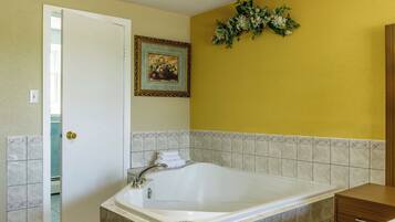 A bathroom with a large bathtub, a door, a framed picture on the wall, and a decorative plant.