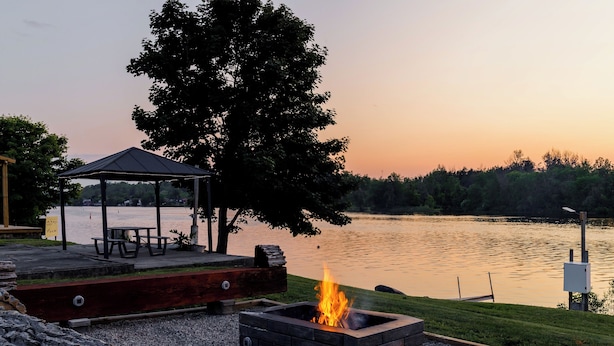 A lakeside outdoor area with a fire pit, picnic table, and gazebo. - Motel 6 Campbellford, ON (Trent Hills)