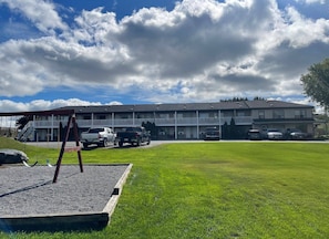 A motel with a two-story building, a parking lot with several cars, and a grassy lawn with a swing set.