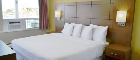 A hotel room with a large bed, two bedside tables, a desk, and a window with curtains.