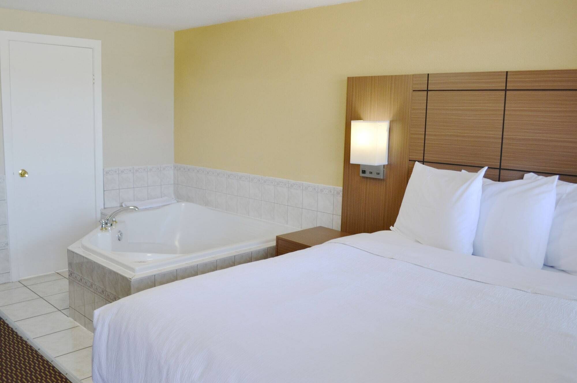 Una camera d'albergo con un letto grande, una vasca da bagno separata e un comodino con una lampada.