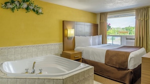 A hotel room with a large bathtub, a bed with a brown blanket, a nightstand, and a view of greenery outside. - Motel 6 Campbellford, ON (Trent Hills)