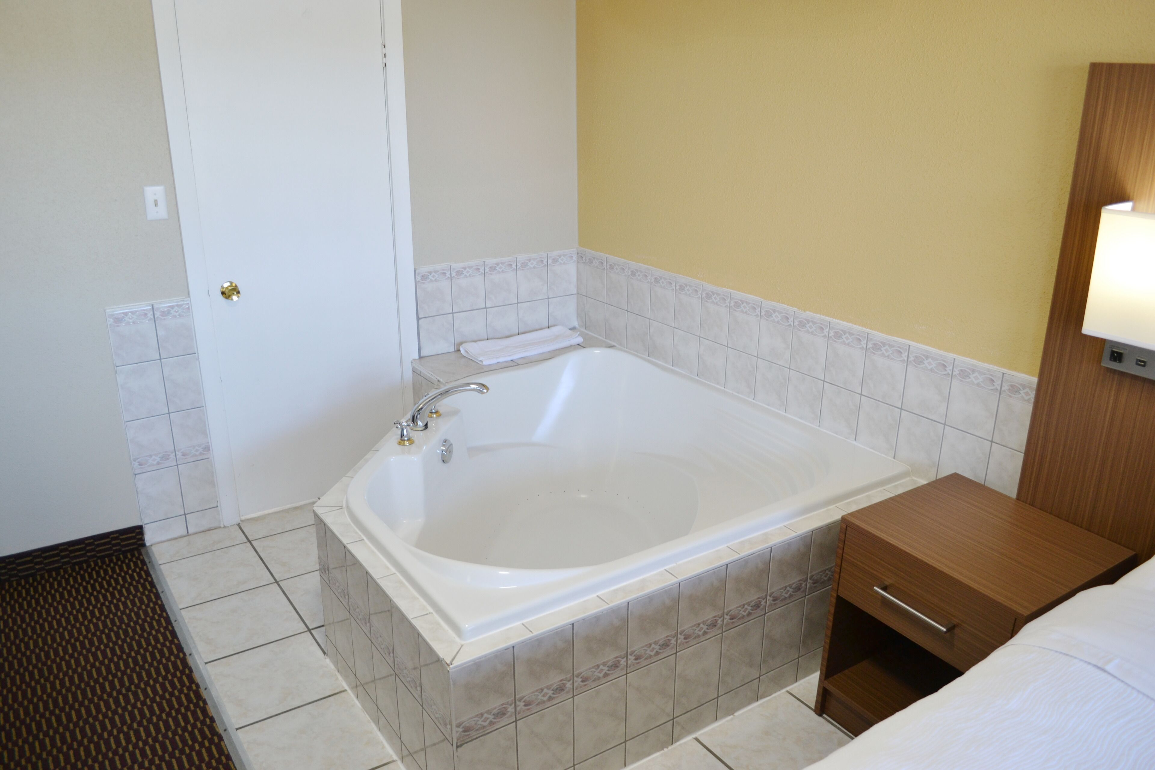 Un bagno moderno con una vasca da bagno ampia, un comodino in legno e una lampada a parete.