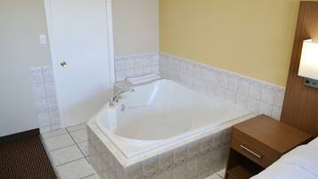 Un bagno moderno con una vasca da bagno ampia, un comodino in legno e una lampada a parete.