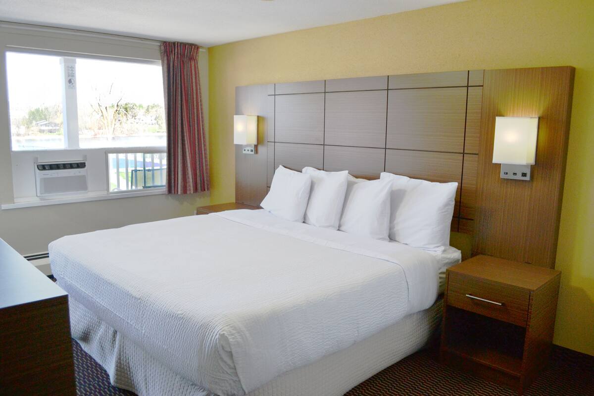 Una habitación de hotel con una cama grande, una mesita de noche, cortinas en la ventana y una lámpara fijada a la pared.
