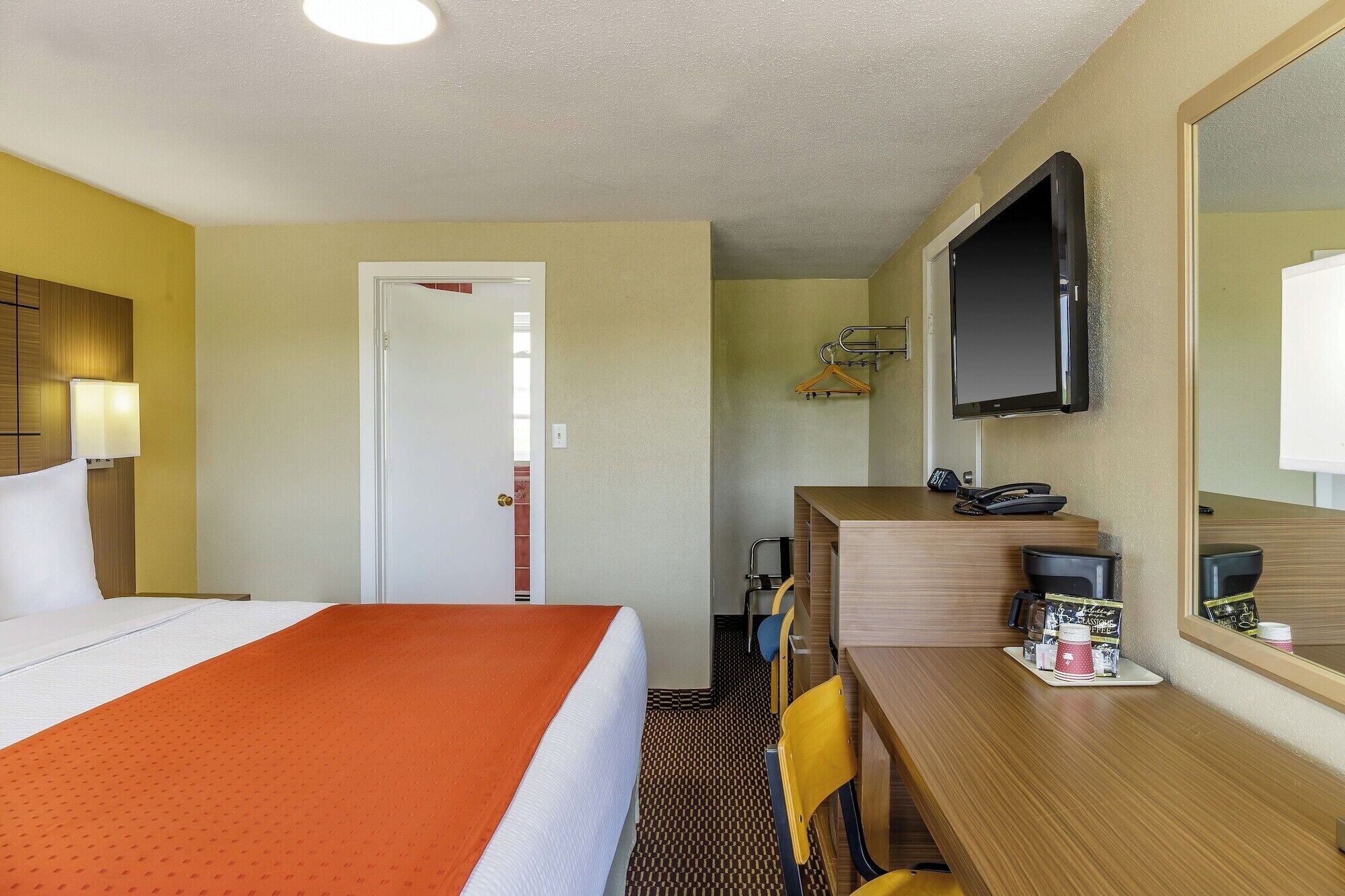 Habitación de hotel con cama, escritorio con teléfono y una taza de café, televisión montada en la pared y una puerta que da a otra habitación.