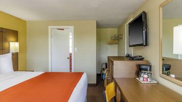 Habitación de hotel con cama, escritorio con teléfono y una taza de café, televisión montada en la pared y una puerta que da a otra habitación.