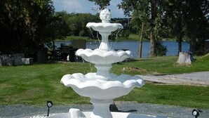 A white, multi-tiered fountain with water cascading down, surrounded by white pebbles and two small lights. - Motel 6 Campbellford, ON (Trent Hills)