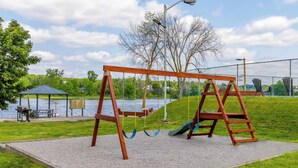 A wooden swing set on a gravel platform with a view of a lake and park benches in the background. - Motel 6 Campbellford, ON (Trent Hills)