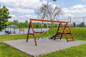 Un columpio de madera sobre una base de grava, con vistas a un lago y bancos de parque al fondo.