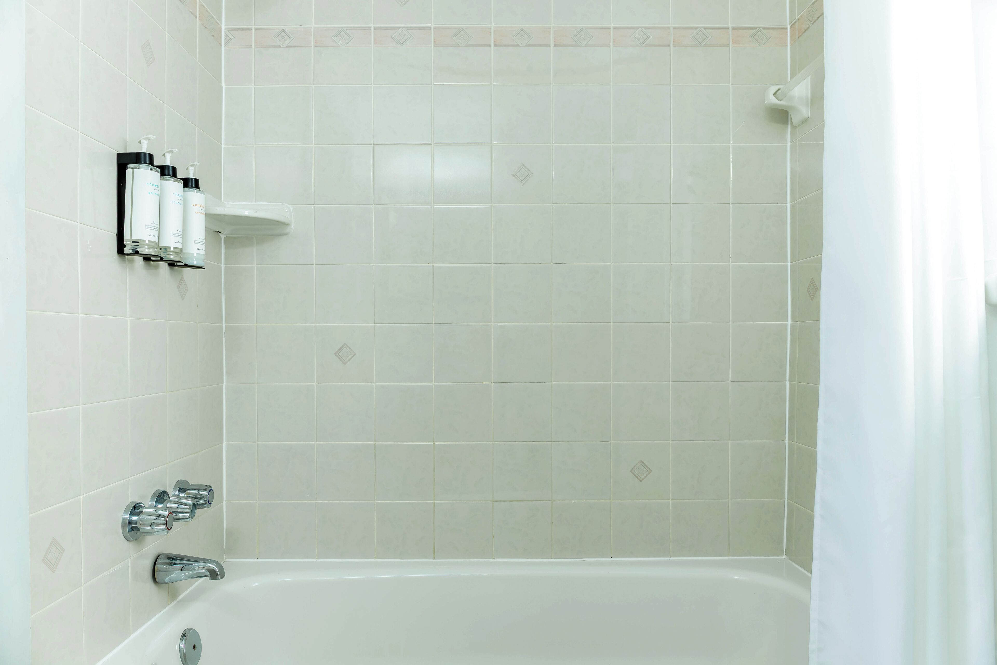 Un baño con una bañera blanca, zona de ducha y un estante con artículos de aseo.