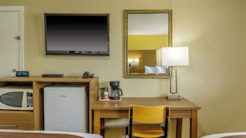 Ein Hotelzimmer mit einem Bett, einem Schreibtisch mit Stuhl, einer Mikrowelle, einem Kühlschrank, einem Fernseher, einer Lampe und einer Uhr.