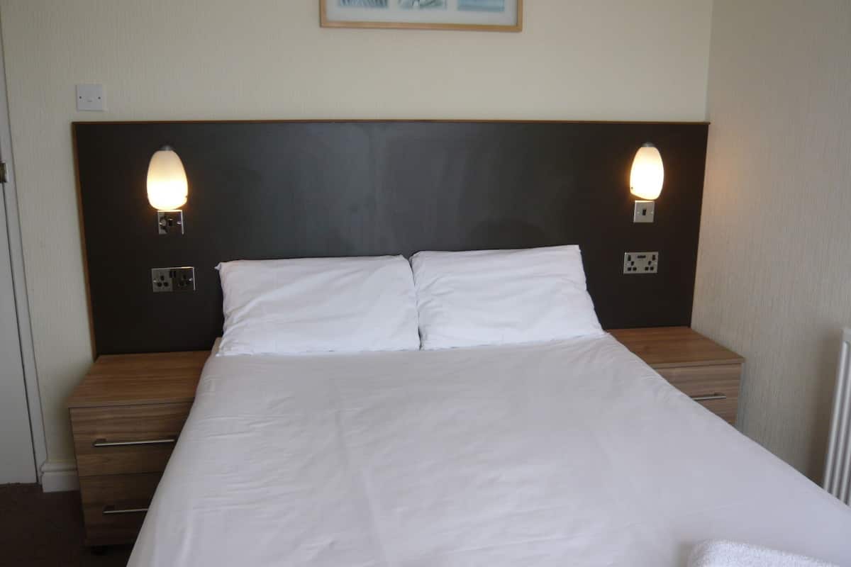A neatly made bed with white linens, two bedside lamps, and a framed picture above the headboard.