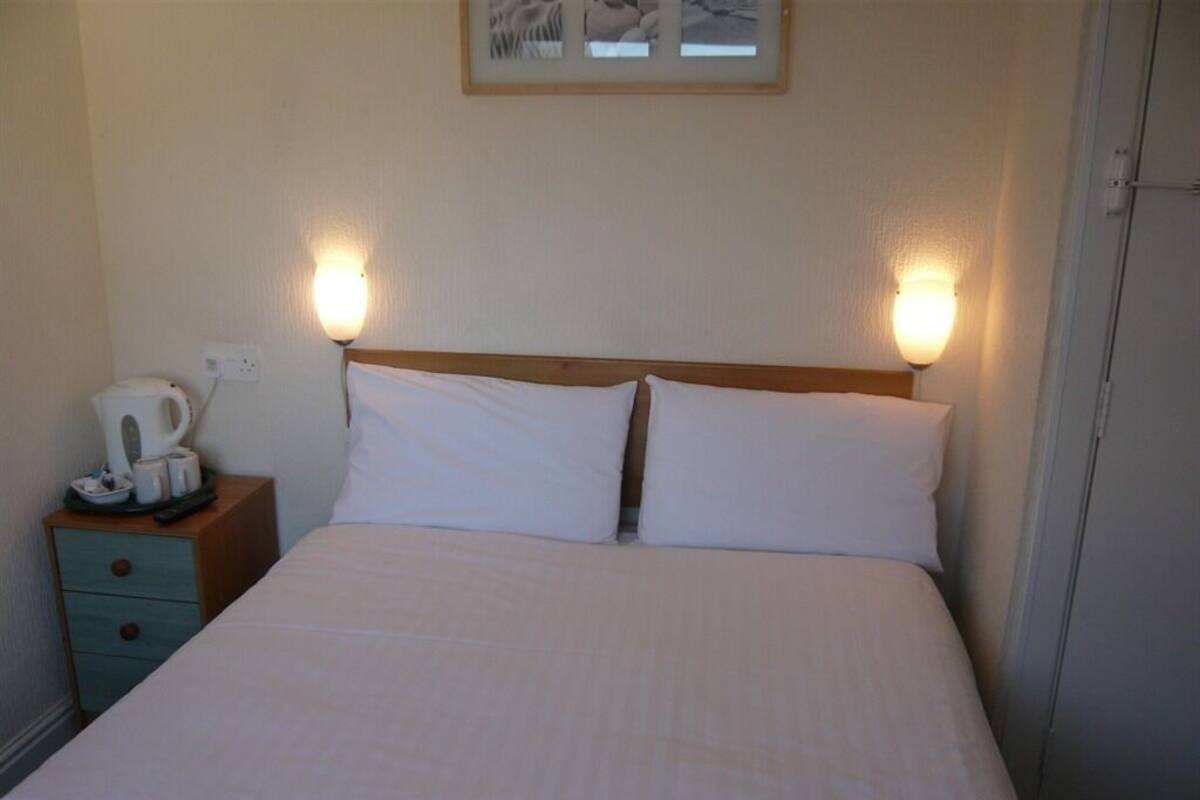 A neatly made bed with white linens, a wooden headboard, and two bedside lamps.