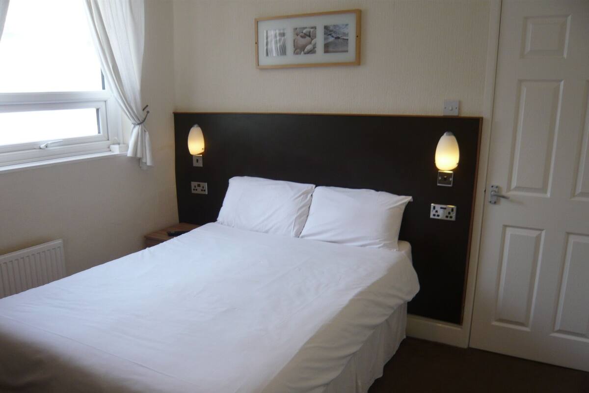A neatly made bed in a hotel room with a dark headboard, two bedside lamps, and a framed picture on the wall.
