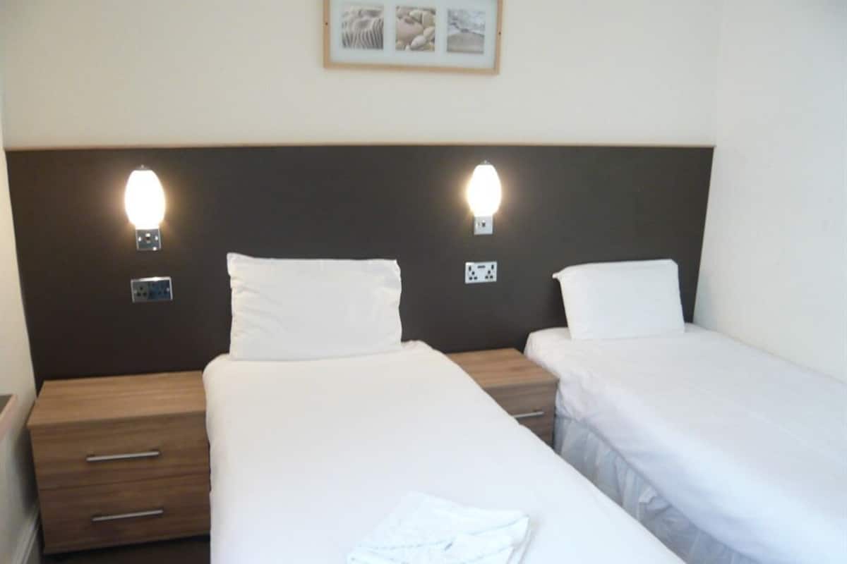 A hotel room with two single beds, each with a wooden nightstand and a drawer.
