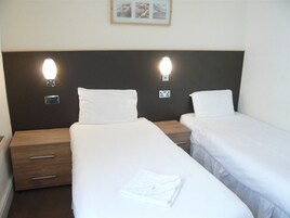 Een hotelkamer met twee eenpersoonsbedden, elk met een houten nachtkastje en een lade.