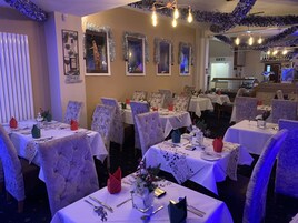 Un restaurante con varias mesas dispuestas para comer, adornadas con centros de flores y cubertería ordenada.