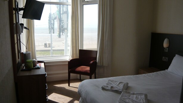A hotel room with a bed, a chair, a desk with a monitor, and a window with curtains. - Dutchman Hotel (Blackpool)