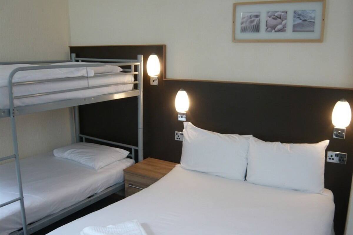 A hotel room with bunk beds, a large bed, bedside lamps, and framed pictures on the wall.