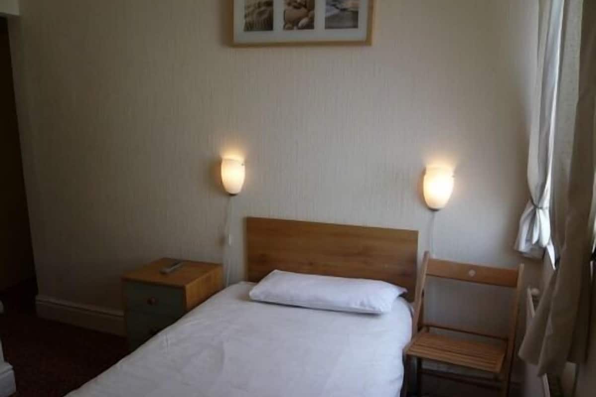 A single bed with a wooden headboard, two bedside tables, and wall-mounted lights.