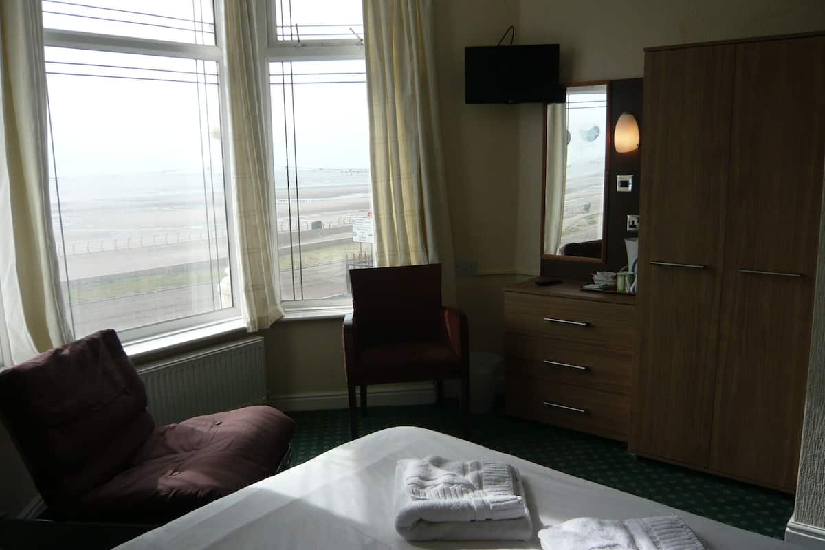 A hotel room with a bed, a chair, a dresser, a television, and a view of the airport.
