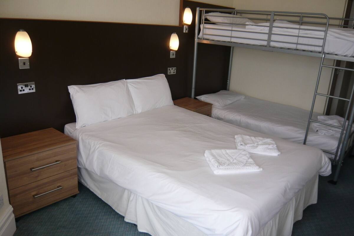 A hotel room with a single bed, a wooden nightstand, a dresser, and a bunk bed.
