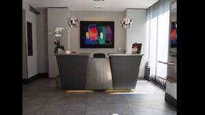 A reception area with a modern design, featuring a reception desk, a large abstract painting, and two pendant lights. - Hôtel Le Carrosse (Paris)