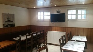 A dining area with wooden booths and tables, a white radiator, and a television mounted on the wall. - Hôtel Le Carrosse (Paris)