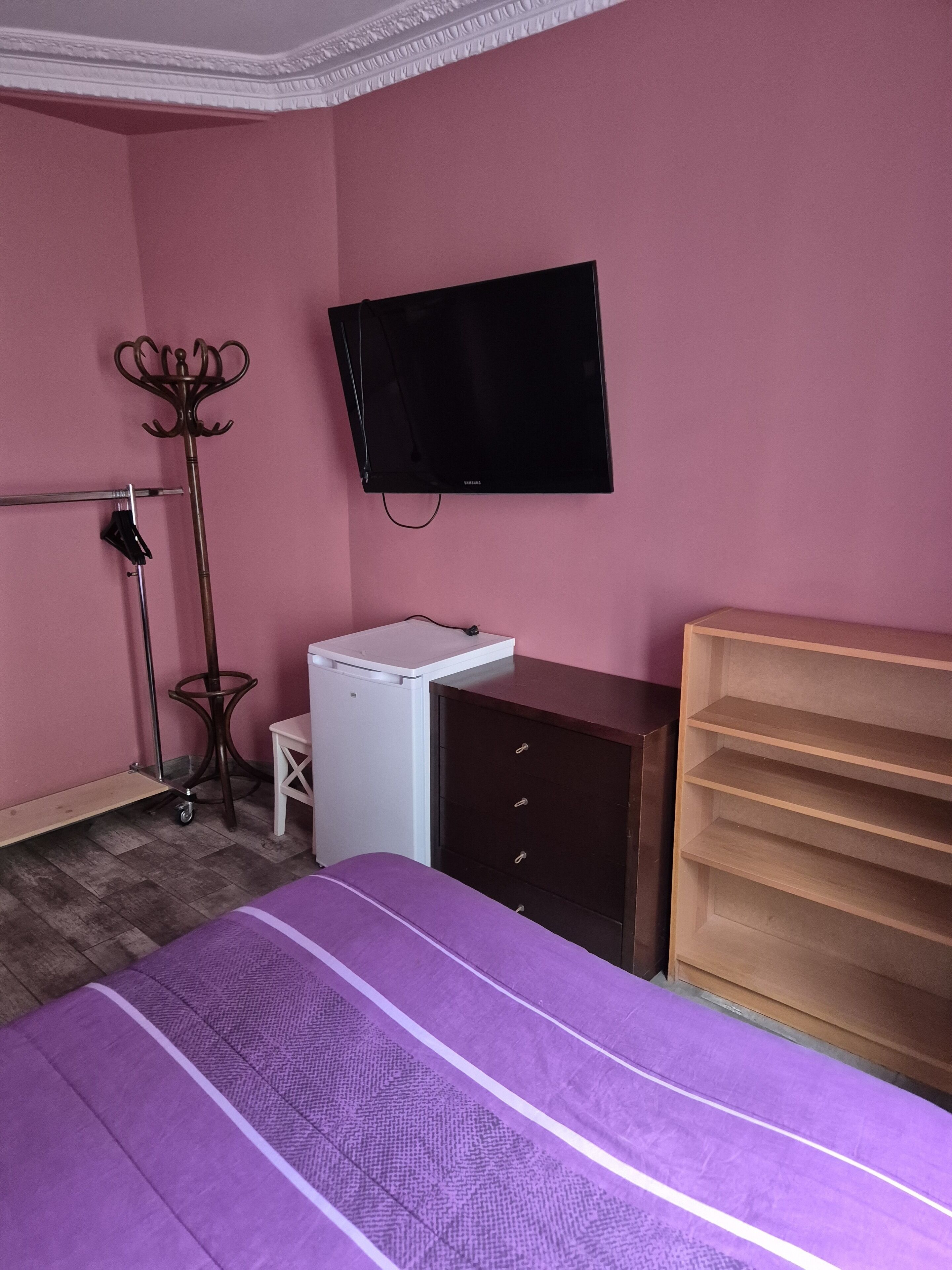 Une chambre à coucher comprenant un lit, un téléviseur fixé au mur, une commode et un bureau.